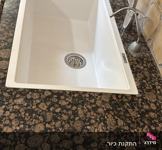 כיור לבן על משטח שיש כהה עם ברז כסוף